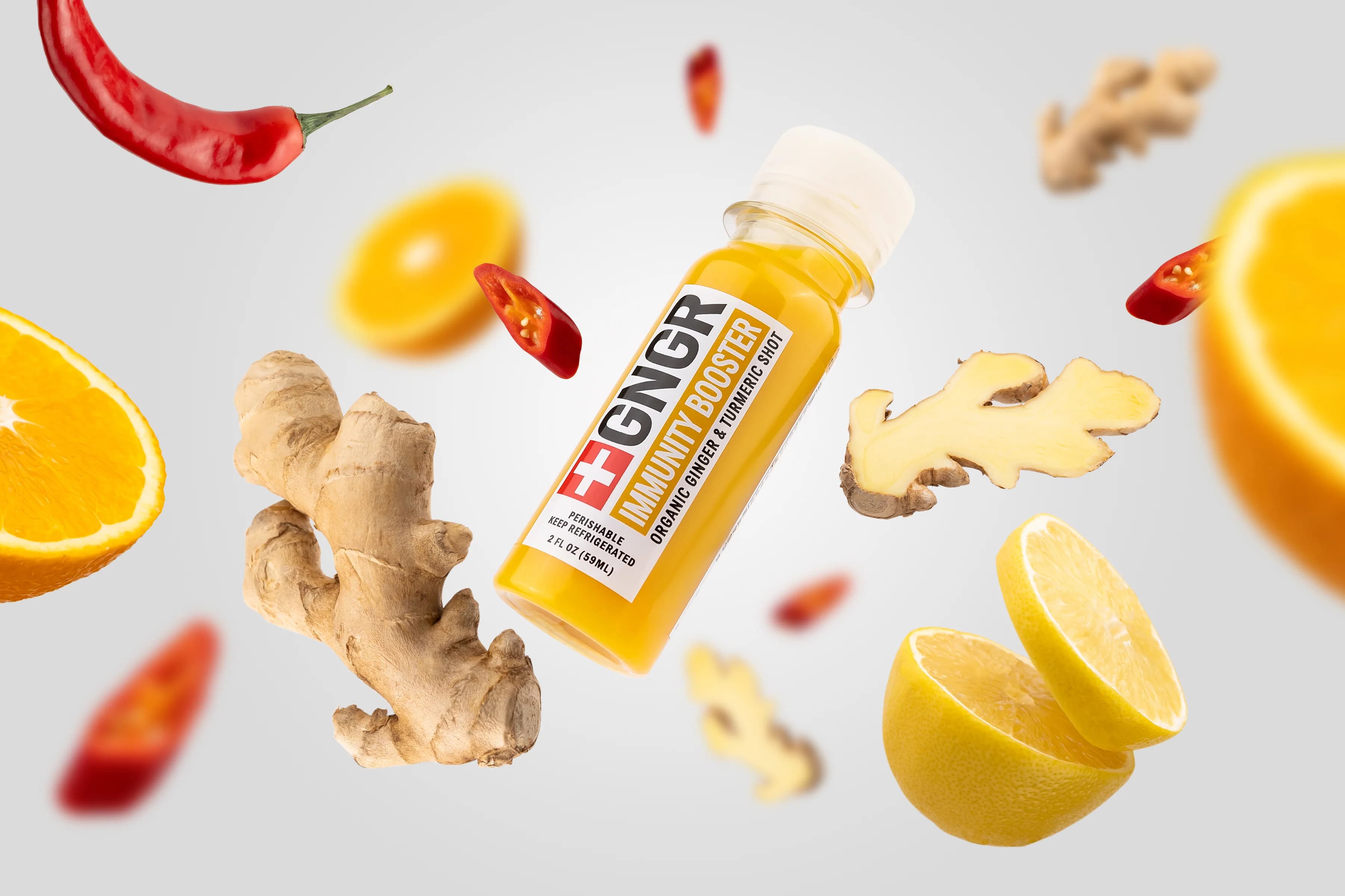 GNGR Labs immunity shot bottle surrounded by flying ginger, lemon, orange, and chili