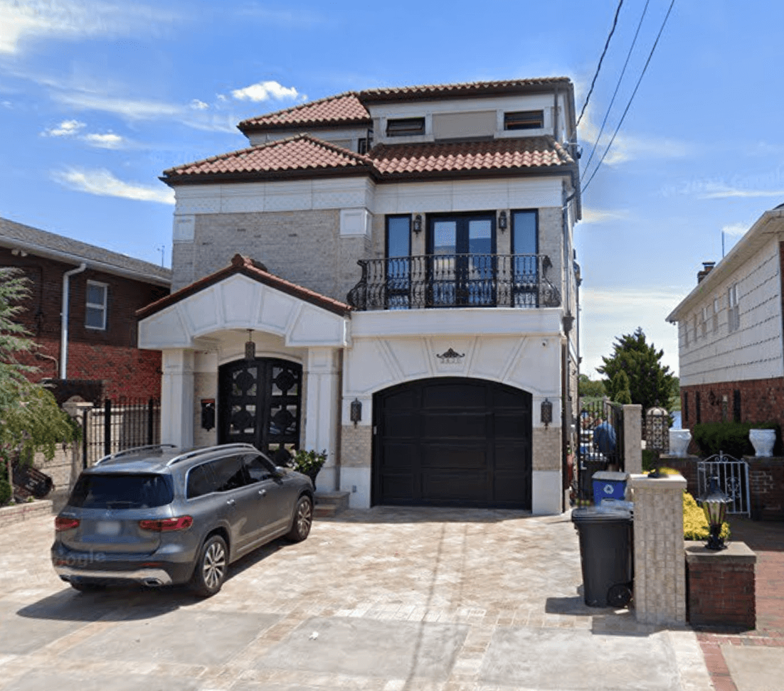 Three-story stucco house with a tile roof, iron balcony, and paver driveway