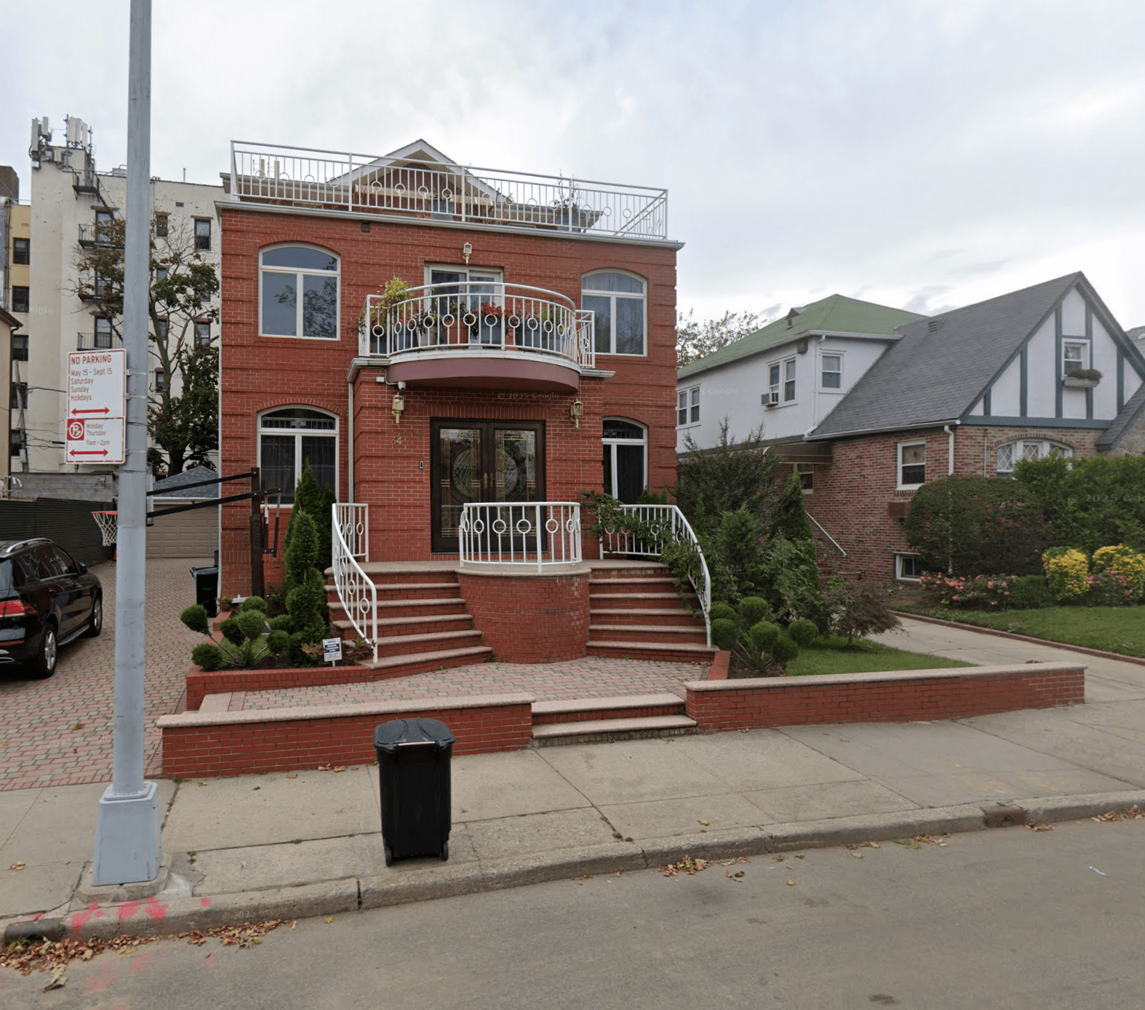 Two-story brick house with a curved balcony and double staircase on a Brooklyn street