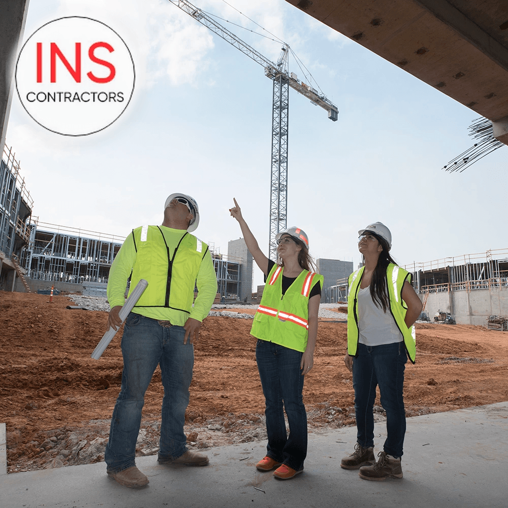 Three INS Contractors crew members in safety vests on a construction site under a tower crane