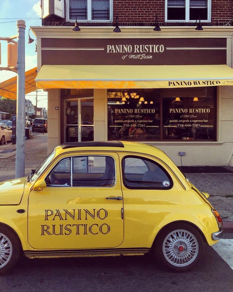 Panino Rustico's yellow vintage Fiat parked in front of the cafe's awning in Mill Basin